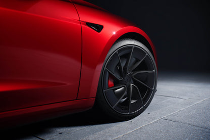 Close-up of a red Tesla Model 3 car with black wheels on a dark background